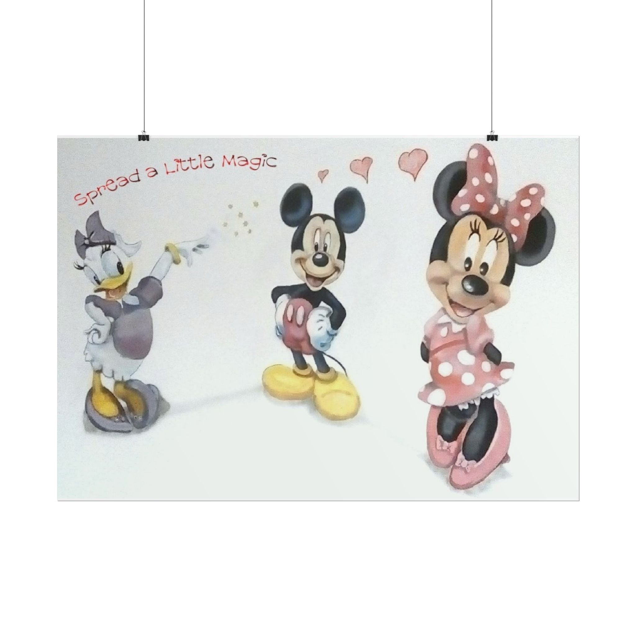 A rectangular wall art print featuring Disney characters Mickey Mouse, Minnie Mouse, and Daisy Duck on a white background, with the text 'Spread a little Magic' and small pink hearts. The print is shown hanging from two black wires against a white wall.